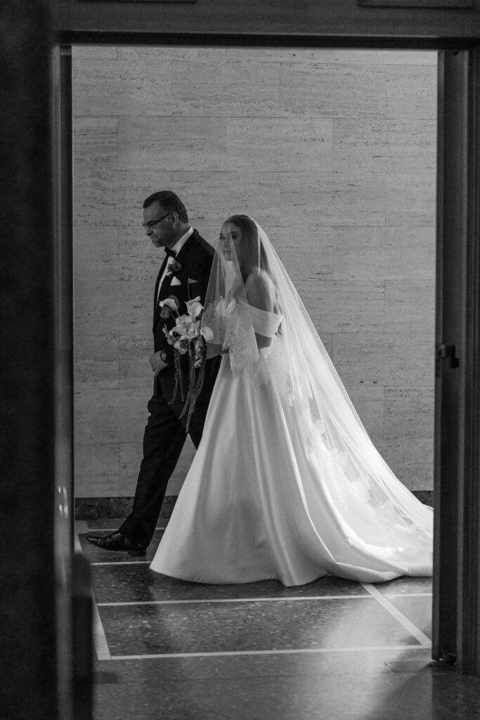Bride and father of the bride walking through church hallway before ceremony.