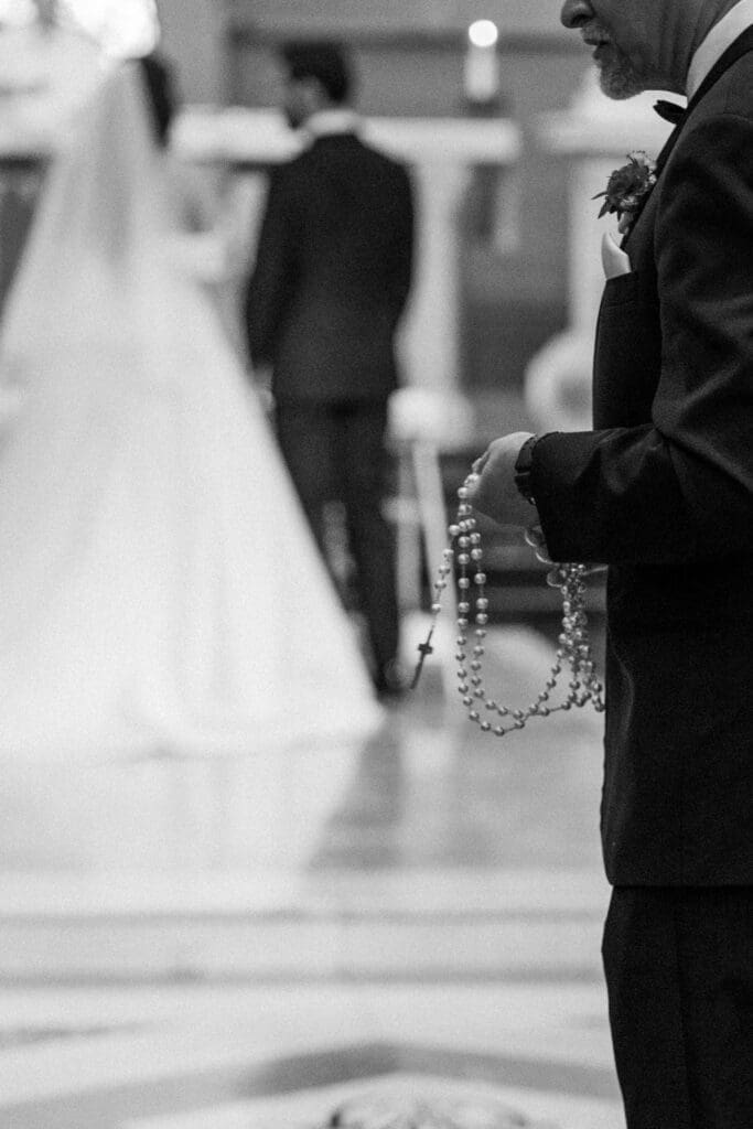 Ceremony details, groomsmen party holding rosary in black and white.